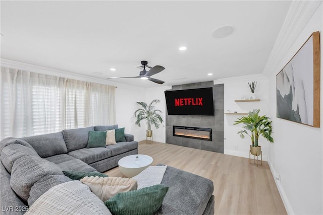 living room featuring light hardwood / wood-style flooring, ceiling fan, ornamental molding, and a fireplace