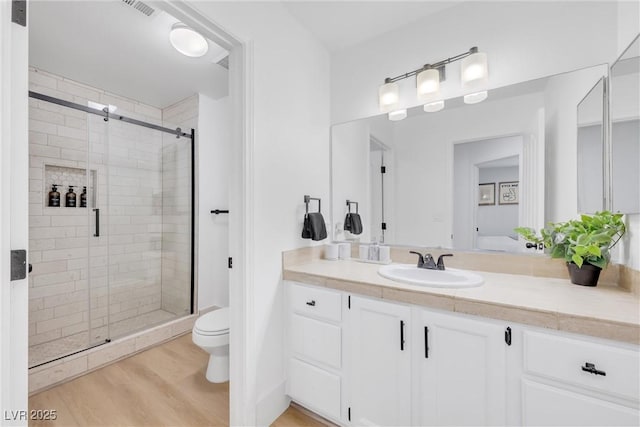 bathroom with toilet, hardwood / wood-style flooring, a shower with shower door, and vanity