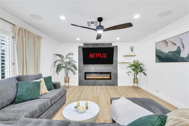 living room featuring hardwood / wood-style floors, ceiling fan, crown molding, and a fireplace