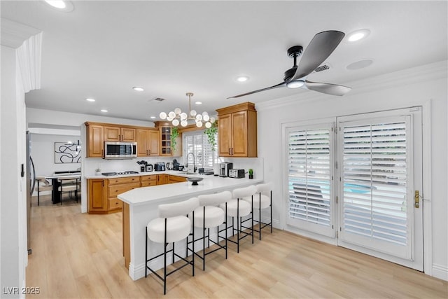 kitchen featuring light wood-type flooring, kitchen peninsula, hanging light fixtures, a breakfast bar, and appliances with stainless steel finishes