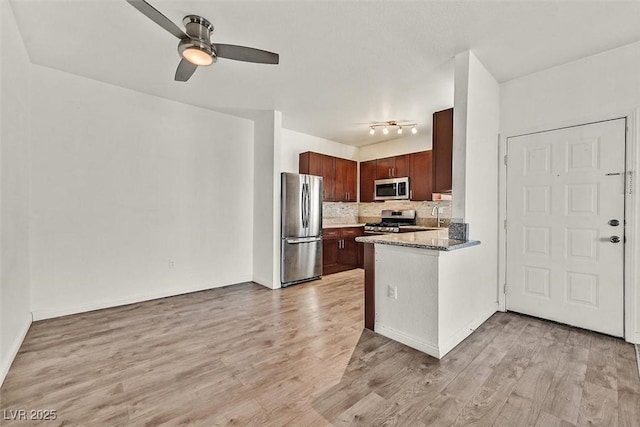 kitchen with backsplash, dark stone counters, ceiling fan, stainless steel appliances, and light wood-type flooring