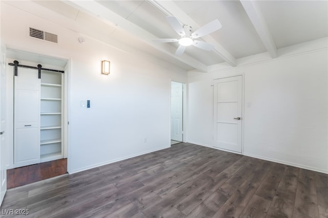 unfurnished bedroom featuring a barn door, dark hardwood / wood-style floors, and vaulted ceiling with beams