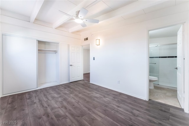 unfurnished bedroom featuring connected bathroom, dark hardwood / wood-style floors, a closet, beamed ceiling, and ceiling fan