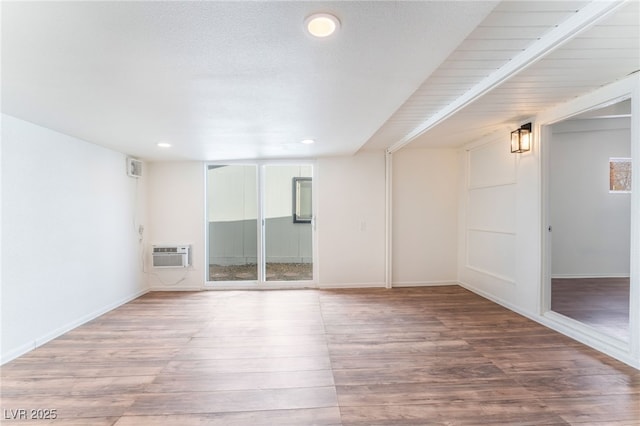 empty room featuring a wall mounted air conditioner, a wealth of natural light, wood-type flooring, and a textured ceiling