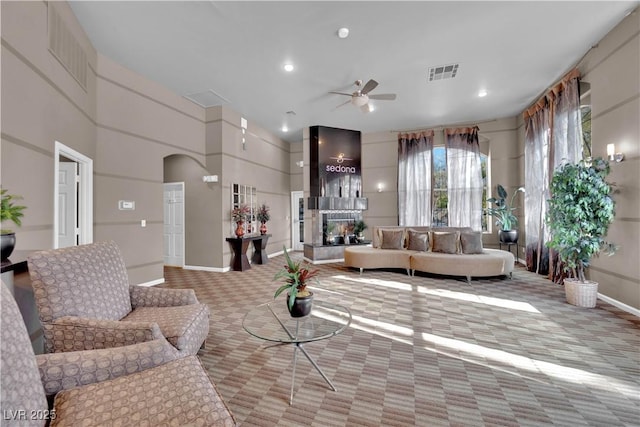 carpeted living room featuring ceiling fan, a towering ceiling, and a fireplace