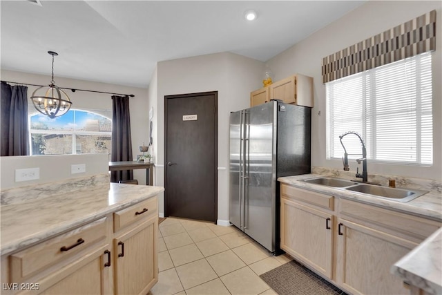 kitchen with light tile patterned flooring, light brown cabinetry, decorative light fixtures, sink, and stainless steel fridge