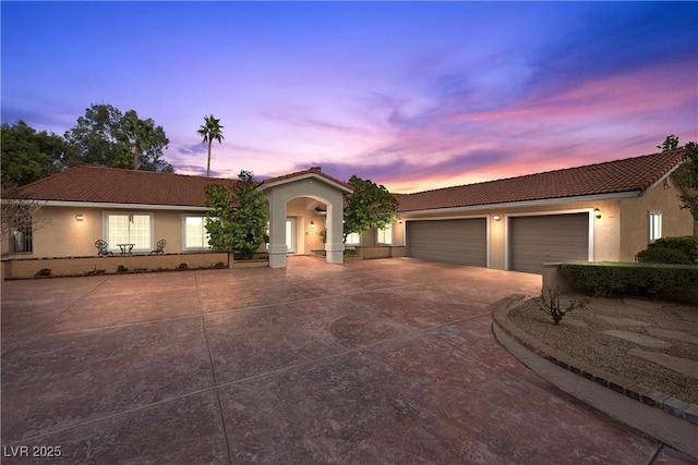 view of front of home featuring a garage, driveway, a tile roof, and stucco siding