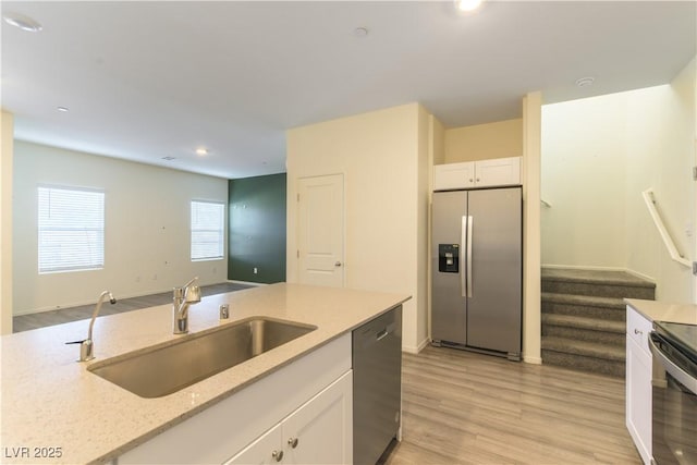 kitchen featuring light stone counters, stainless steel appliances, a sink, white cabinets, and light wood finished floors