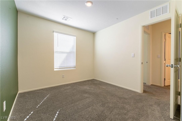 spare room featuring dark carpet, visible vents, and baseboards