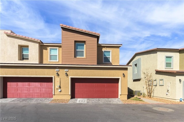 townhome / multi-family property with central AC unit, an attached garage, and stucco siding