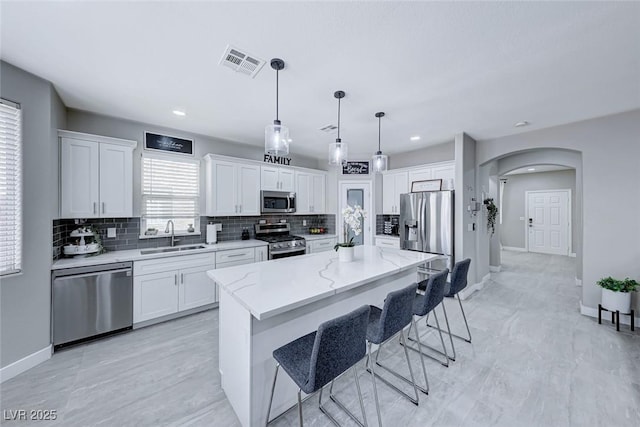 kitchen featuring sink, a center island, appliances with stainless steel finishes, pendant lighting, and white cabinets