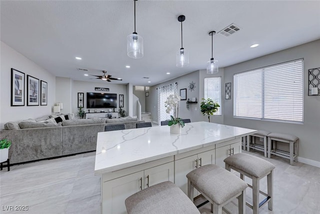 kitchen with white cabinetry, hanging light fixtures, a kitchen bar, light stone counters, and a kitchen island