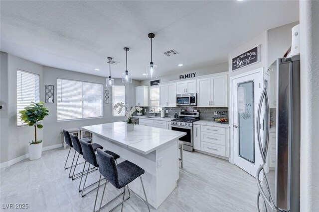 kitchen featuring stainless steel appliances, a kitchen breakfast bar, white cabinets, a kitchen island, and decorative light fixtures