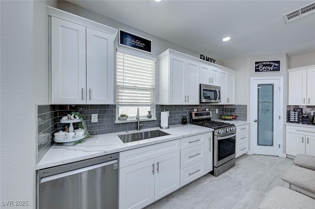 kitchen with sink, white cabinetry, backsplash, stainless steel appliances, and light stone counters