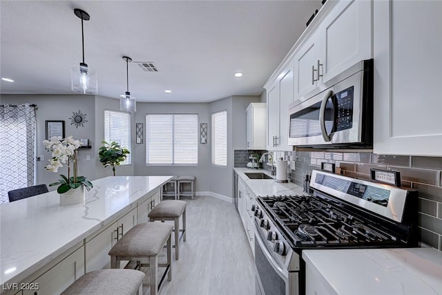 kitchen featuring sink, a breakfast bar area, appliances with stainless steel finishes, white cabinetry, and light stone counters