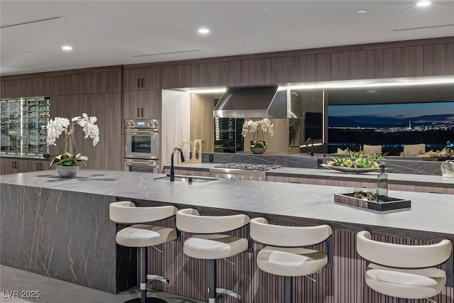 kitchen featuring stainless steel appliances, sink, a breakfast bar area, and wall chimney exhaust hood