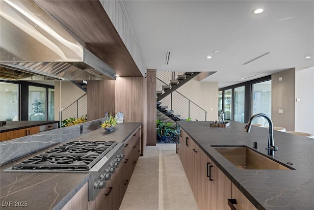 kitchen with sink, wall chimney range hood, dark stone counters, and stainless steel gas stovetop