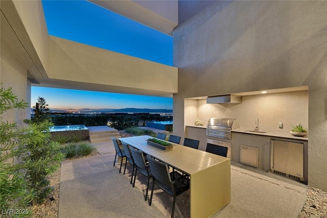 patio terrace at dusk featuring sink, a mountain view, grilling area, and exterior kitchen