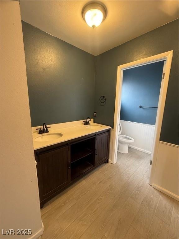 bathroom with wainscoting, toilet, wood finished floors, and a sink