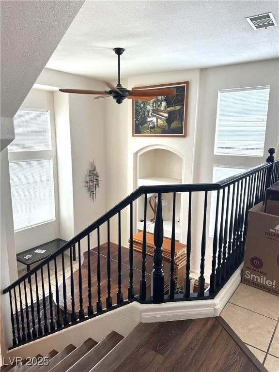 stairs featuring a ceiling fan, wood finished floors, visible vents, and a textured ceiling