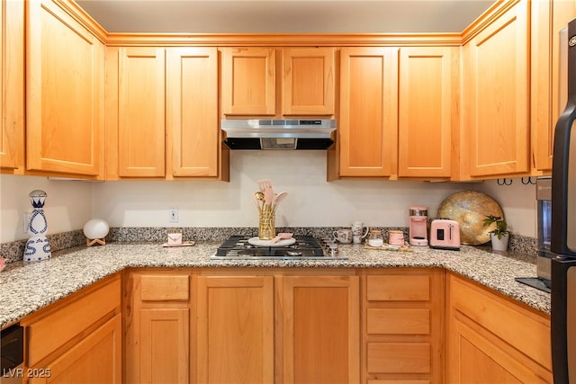 kitchen featuring black fridge, stainless steel gas stovetop, and light stone countertops