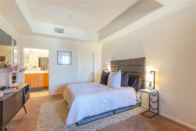 bedroom featuring light carpet, a raised ceiling, and ensuite bathroom