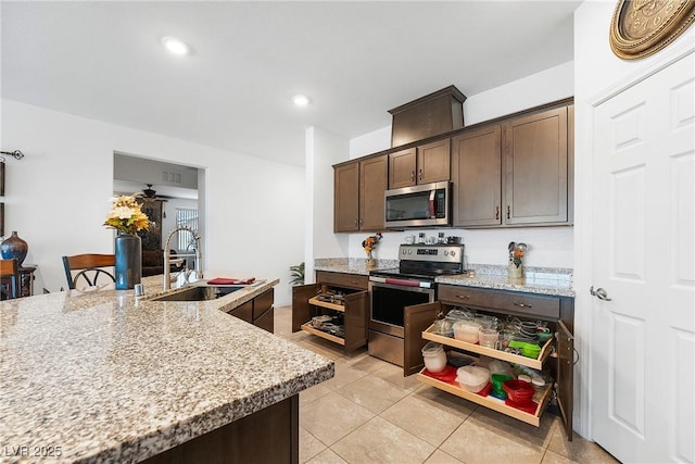 kitchen with light stone counters, stainless steel appliances, light tile patterned flooring, a sink, and dark brown cabinets