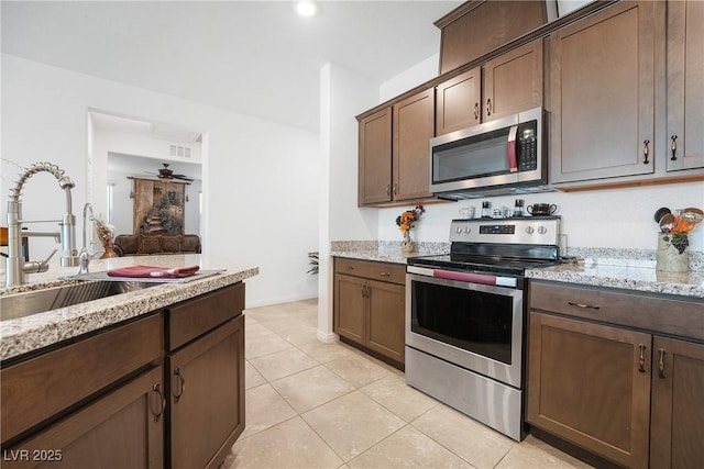 kitchen featuring stainless steel appliances, visible vents, light tile patterned flooring, a sink, and light stone countertops