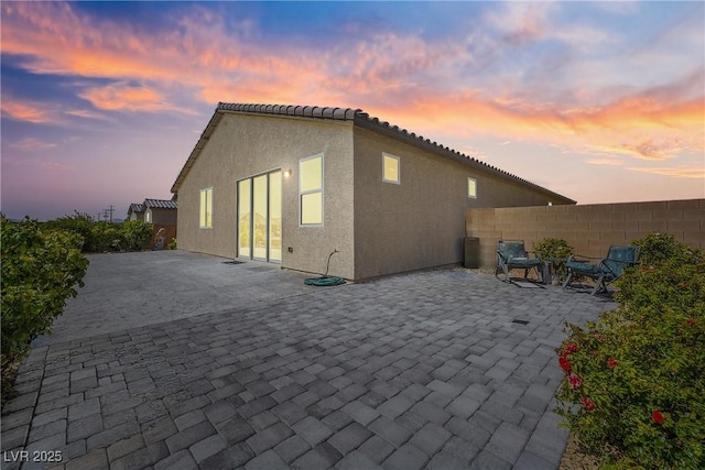 back of property at dusk with a patio area, a tile roof, fence, and stucco siding