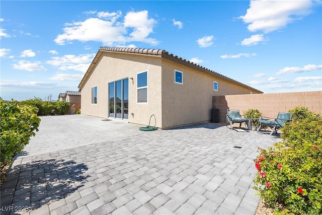 back of property with stucco siding, a tiled roof, fence, and a patio