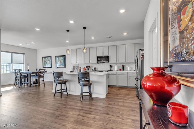 kitchen with pendant lighting, gray cabinets, a kitchen breakfast bar, stainless steel appliances, and an island with sink