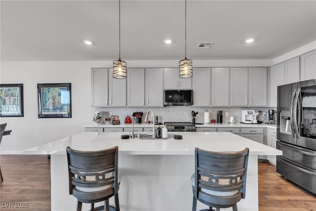 kitchen featuring a kitchen island with sink, pendant lighting, gray cabinets, and appliances with stainless steel finishes