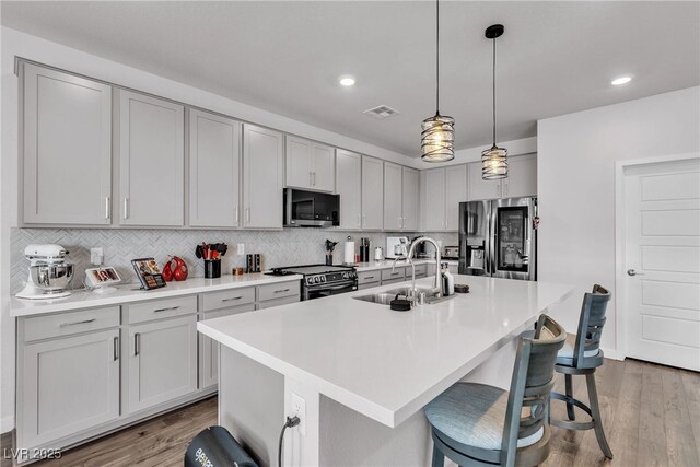 kitchen with decorative light fixtures, a center island with sink, a breakfast bar area, and appliances with stainless steel finishes