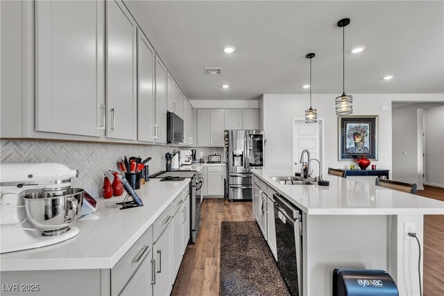 kitchen featuring decorative light fixtures, wood-type flooring, sink, a kitchen island with sink, and stainless steel appliances