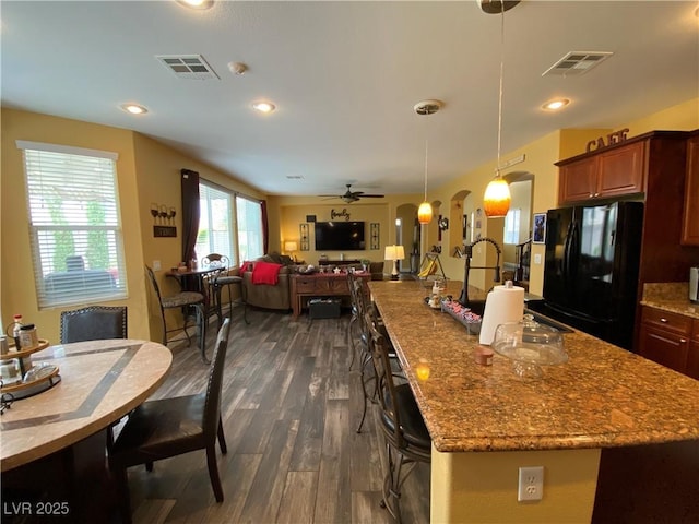 kitchen with dark wood-type flooring, black refrigerator, light stone countertops, a kitchen bar, and decorative light fixtures