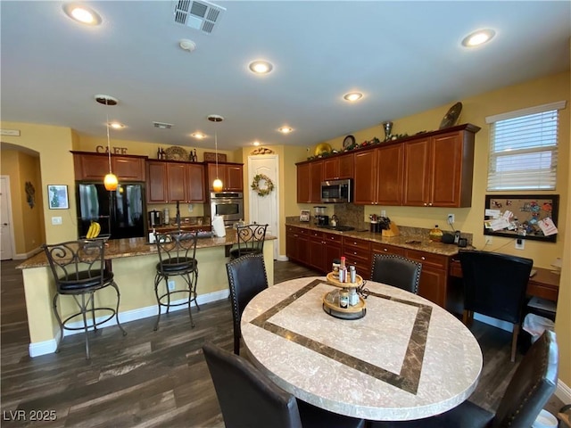 kitchen featuring dark wood-type flooring, a breakfast bar, stainless steel appliances, a kitchen island, and decorative light fixtures