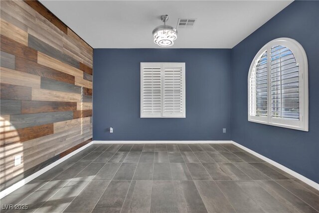 empty room with tile patterned floors, baseboards, visible vents, a chandelier, and wooden walls