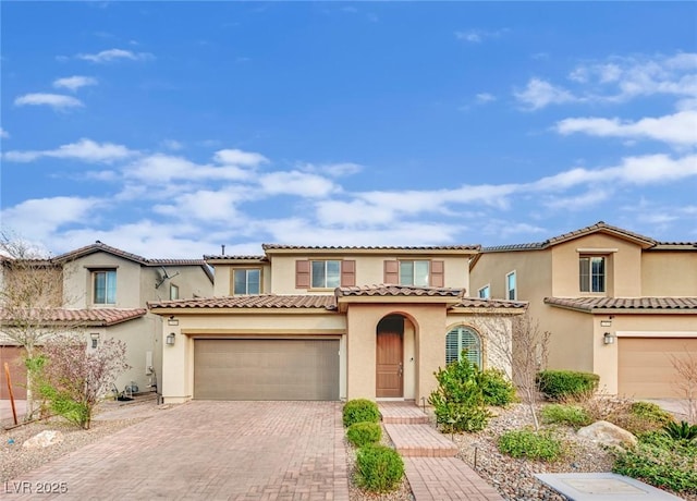 mediterranean / spanish-style house featuring stucco siding, a tile roof, decorative driveway, and a garage