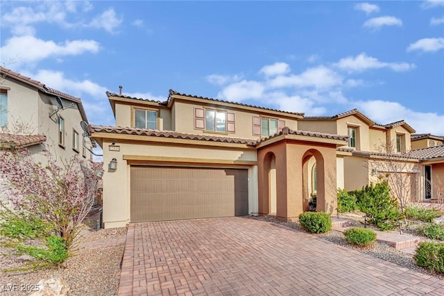 mediterranean / spanish home featuring an attached garage, a tile roof, decorative driveway, and stucco siding