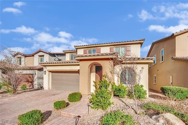 mediterranean / spanish-style house featuring an attached garage, a tiled roof, stucco siding, and decorative driveway