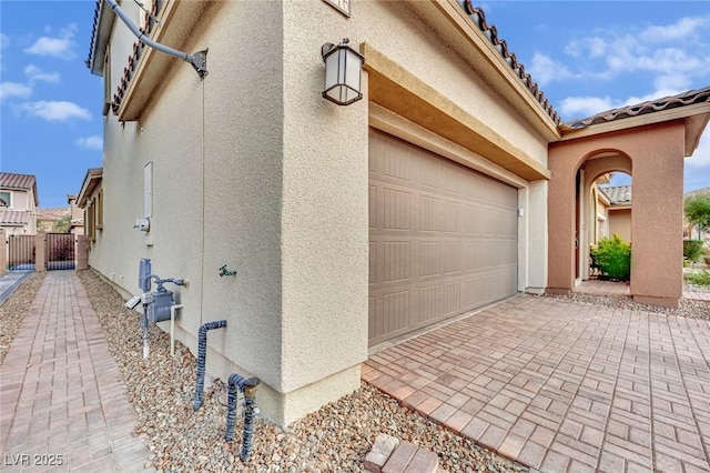 view of home's exterior with stucco siding, decorative driveway, a garage, and a gate