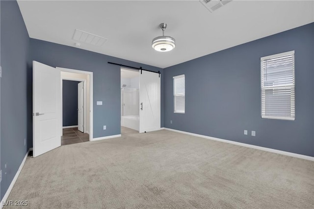 unfurnished bedroom featuring visible vents, connected bathroom, carpet floors, a barn door, and baseboards