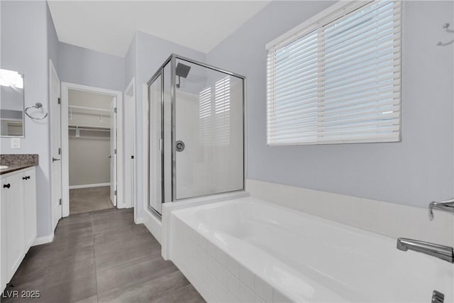 bathroom with a shower stall, vanity, a walk in closet, and a garden tub