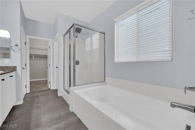 bathroom with a spacious closet, vanity, a garden tub, and a stall shower