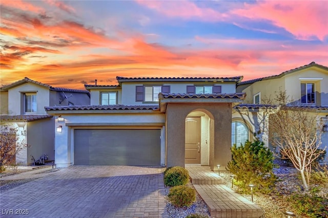 mediterranean / spanish home featuring stucco siding, a tiled roof, an attached garage, and decorative driveway