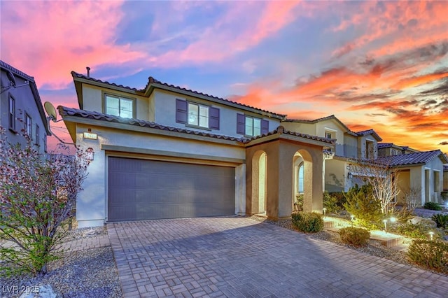 mediterranean / spanish house with a tiled roof, decorative driveway, a garage, and stucco siding