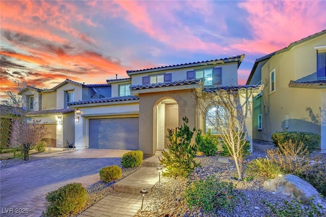 mediterranean / spanish-style house featuring stucco siding, an attached garage, a tiled roof, and decorative driveway