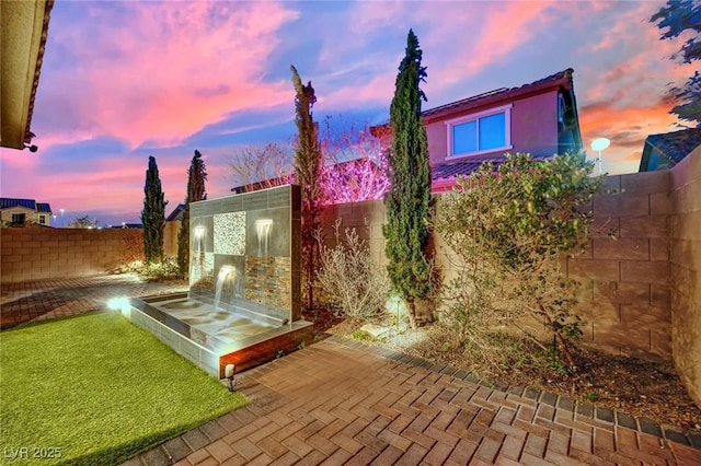 back of house at dusk with stucco siding and a fenced backyard