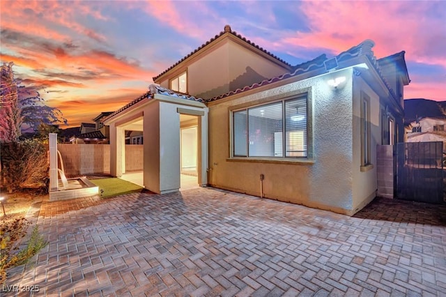 rear view of house featuring stucco siding, a patio, fence, and a tile roof