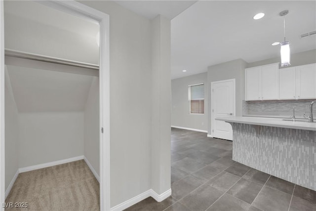 kitchen with baseboards, light countertops, pendant lighting, white cabinetry, and backsplash